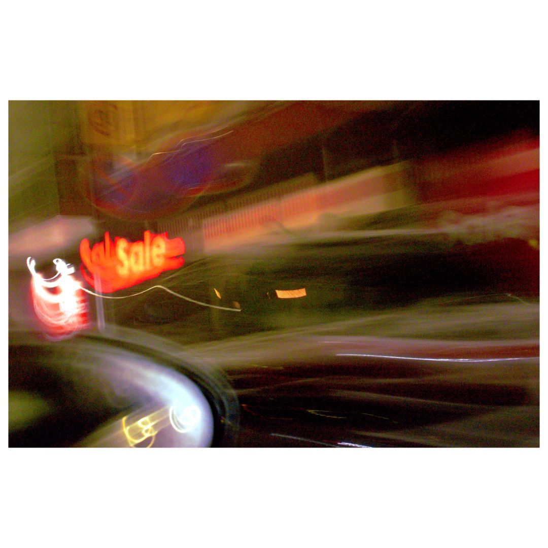 A blurred nighttime city scene featuring a glowing red sign that reads 