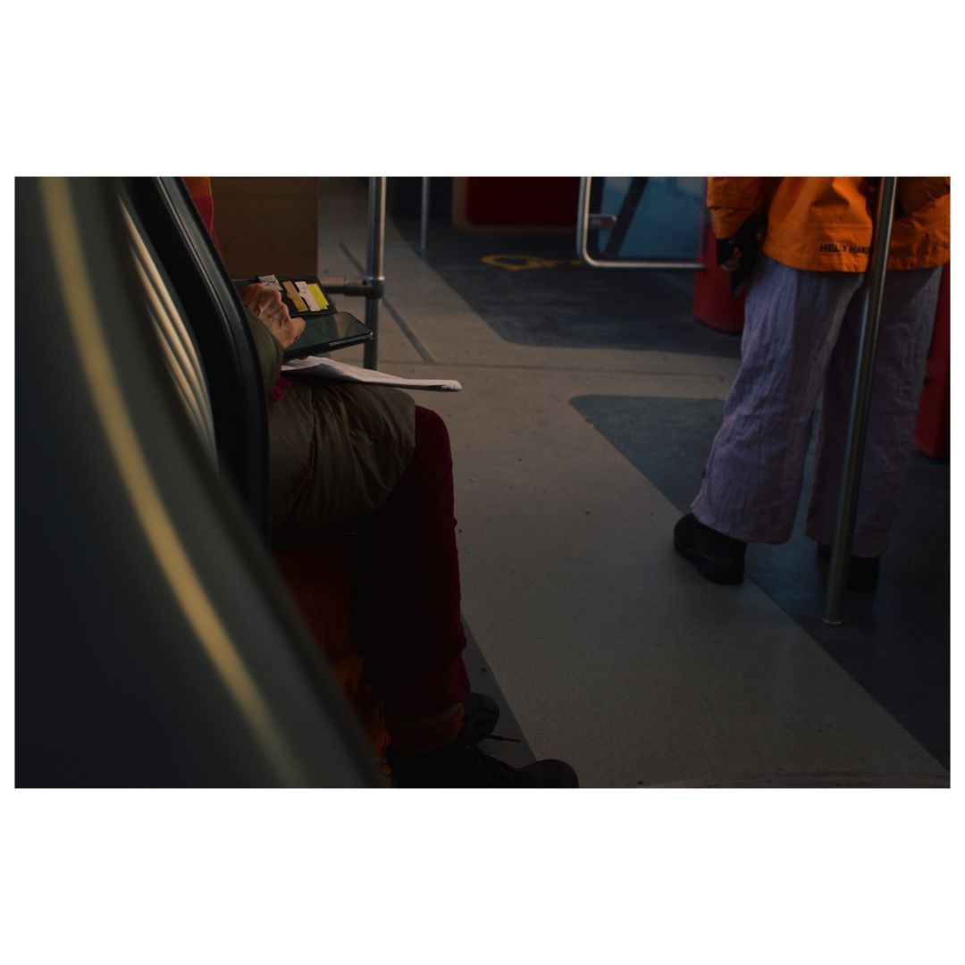 An interior view of a tram showing a person seated, holding a phone, with another individual standing in the background.