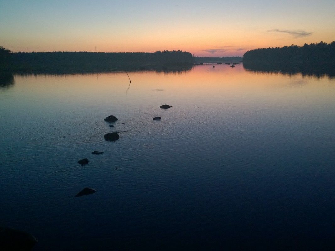 Sea in sunset, a few rocks on foreground. Islands and mainland on the background.