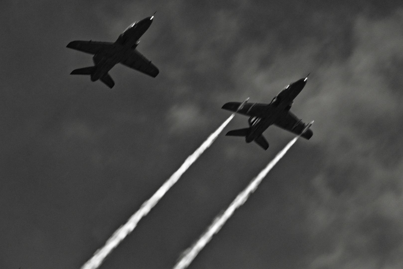 Two BAE Systems Hawk advanced trainer airplanes flying overhead. One plane is leaving back trails.