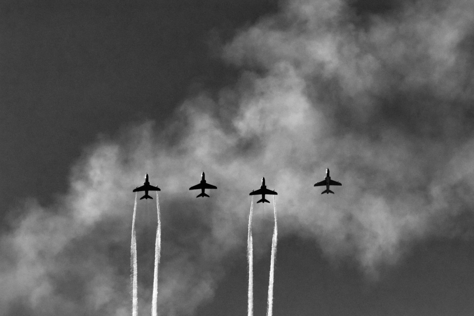 Four BAE Systems Hawk advanced trainer airplanes flying overhead. Two plane is leaving back trails.