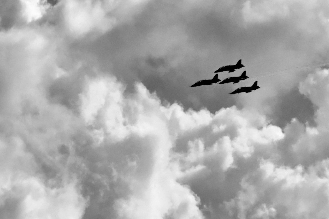 Four BAE Systems Hawk advanced trainer airplanes flying overhead next to the big clump of clouds.