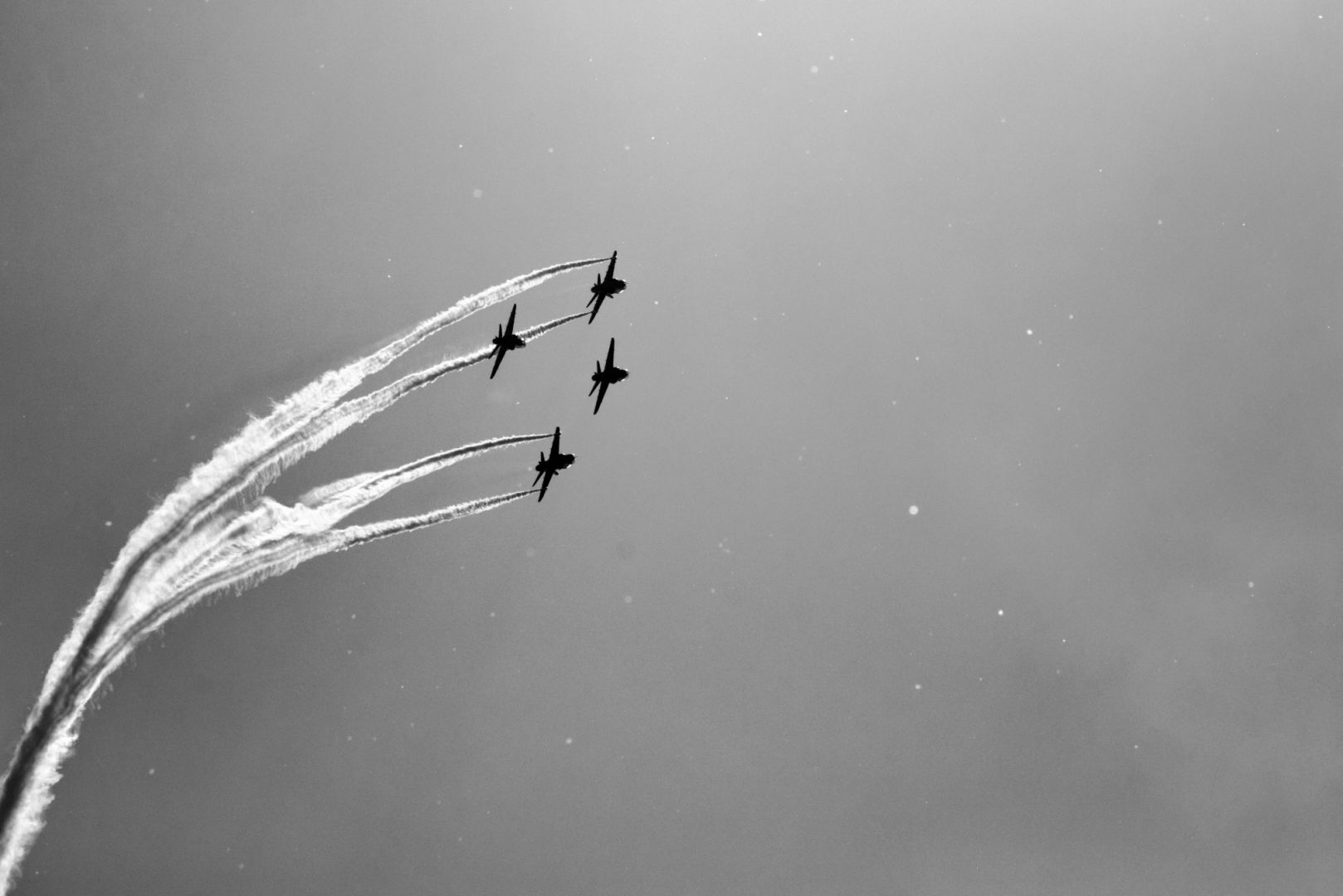 Four BAE Systems Hawk advanced trainer airplanes flying overhead. Two plane is leaving back trails.