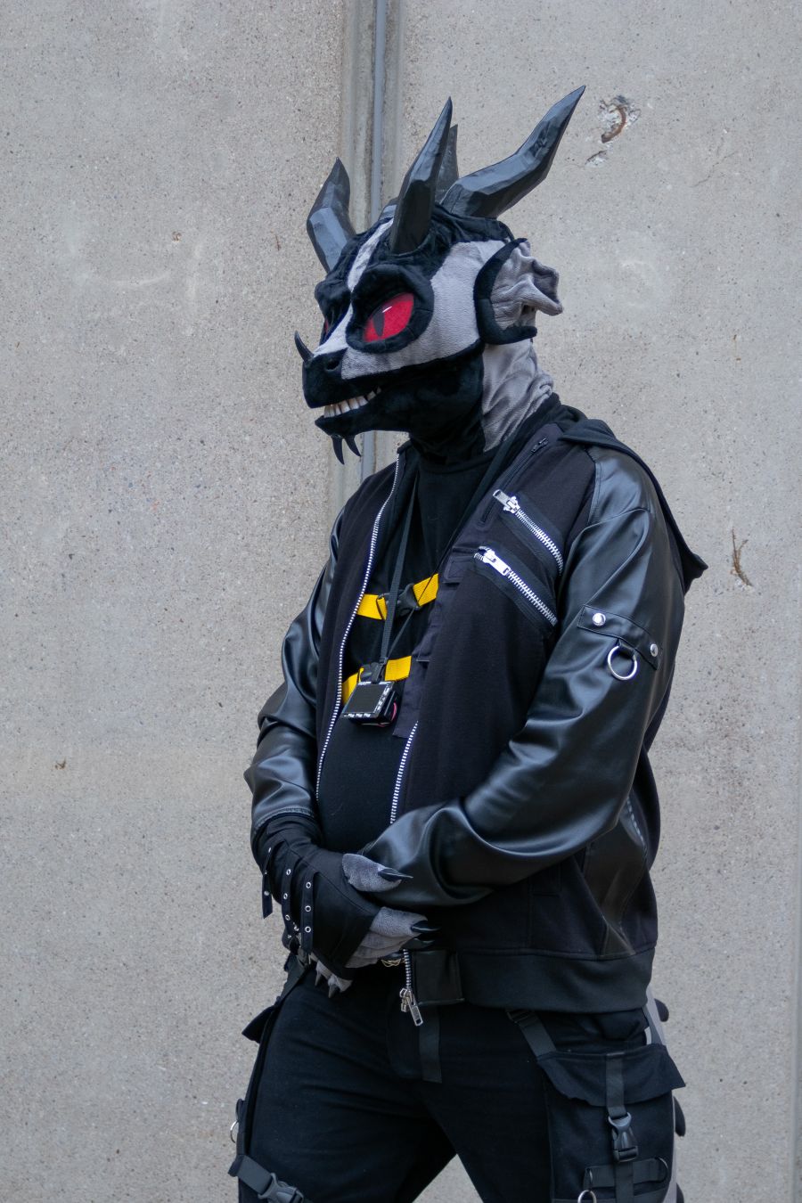 Lizardman cosplay wearing techwear, standing on front of a wall with arms slightly crossed