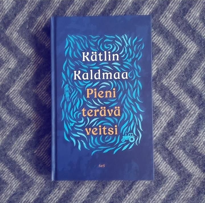 Kuvassa on sininen kirja, jonka kannessa on vaaleamman sinisiä lehtimäisiä kuvioita ja niiden lomassa pieniä hahmoja: tyttö, traktori, jakoavain, perhosia. Kirjan nimi lukee keltaisin kirjaimin ja kirjailijan nimi yllä valkoisin. Kuvaustaustana on siksak-kuvioinen harmaa villapeitto.