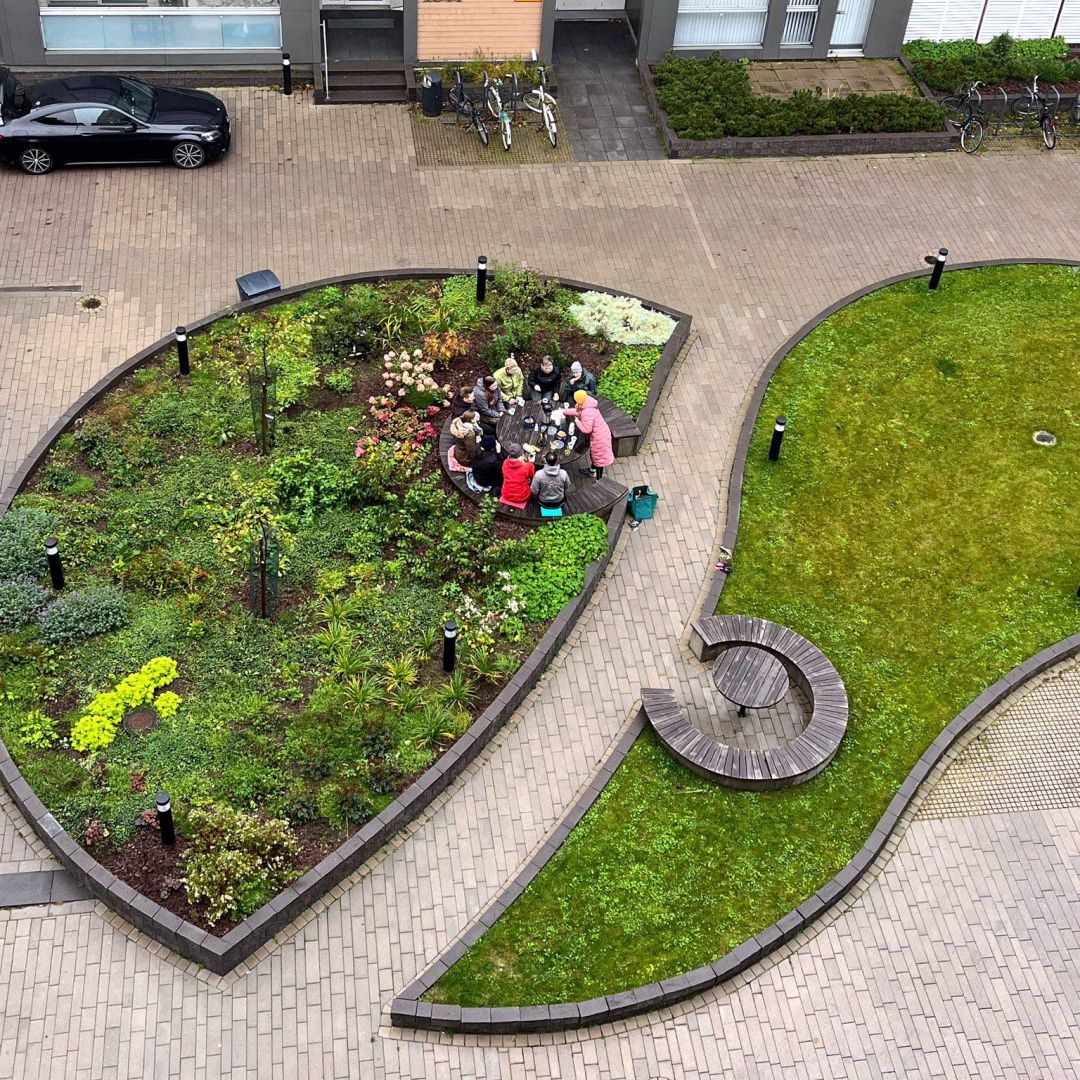 Korkealta ylhäältä otettu kuva, jossa näkyy iso istutusalue ja nurmialue kiveyksen ympäröimänä. Istutusalueen kyljessä on pöytä, jonka ääressä istuu ihmisiä.