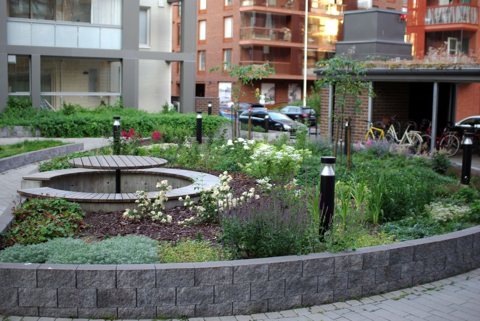 Yleiskuva istutusalueesta, jossa kasvaa runsaasti erilaisia perennoja, pensaita pöytäryhmän ympärillä ja kaksi rautatienomenapuuta.