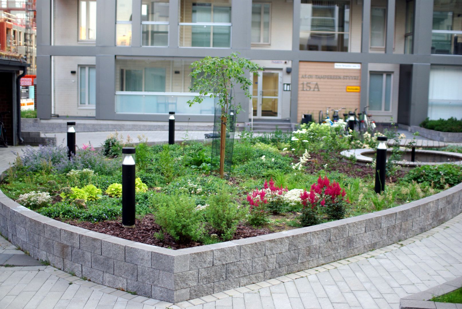 Yleiskuva istutusalueesta, jossa kasvaa runsaasti erilaisia perennoja, pensaita pöytäryhmän ympärillä ja kaksi rautatienomenapuuta.